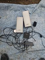 Two silver Bose satellite speakers, control pod and power adapter laid out on a blue blanket, showing entire system including cables.
