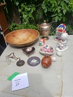 Photo showing all lot items on a table including wooden bowl, copper pot, Precious Moments figurine, tiny Coke bottle, Stimpy and Paddington Bear figures, Olympic pendant, and other collectibles.