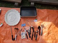 Roasting pan, ceramic turkey platter, ceramic chicken-shaped egg holders, and assorted cooking utensils laid out on orange tarp.