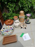 Overview photo of entire lot showing all ceramic, wooden and pottery items arranged outdoors on a table.