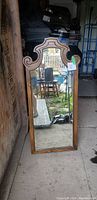 Front view of a tall wood hanging mirror with curved decorative top edges and a natural wood frame.
