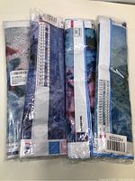 Four diamond painting kits sealed in plastic displaying partial canvases with numeric charts, stacked side by side on a flat surface.