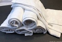 Six white rolled towels stacked with one towel partially unfolded, showing texture and edges.
