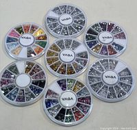 Seven circular plastic wheels labeled VAGA containing assorted small nail art decorative pieces in various colors and shapes arranged in compartments.