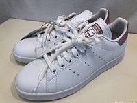 Angled side-front view of the white leather Adidas Stan Smith sneakers with laces tied and visible tags.