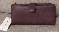 Closed view of plum coloured Matt & Natt wallet showing smooth textured synthetic leather and zipper top.