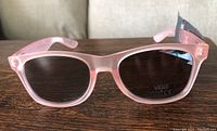 Close-up front view of pink translucent Vans sunglasses with dark lenses showing UV400 sticker.
