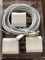 Photo of three new white Lightning charging cables and three white USB power adapter cubes packaged together in a clear plastic tray.