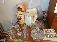 Overall lot showing metal canisters with red fruit designs, various clear glass candle holders, glass candy dish with lid, ceramic napkin rings, napkins, and metal accessories.