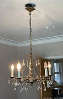 Full view of the chandelier hanging from the ceiling showing five candle-style lights with glass prisms and metal frame