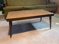 Front angle view of rectangular wood veneer coffee table with four tapered legs and brass caps.
