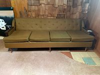 Photo of front view of green, button-tufted four-cushion couch with mid-century wooden legs and wood armrests