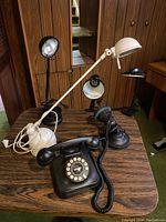Entire lot on wood table showing four different desk lamps in black and white finishes and a vintage style black rotary phone in front.
