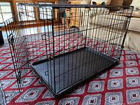 Black collapsible metal dog crate set up and empty, placed on a patterned rug indoors