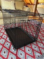 Black metal wire collapsible dog crate set up on carpet indoors, showing one door and plastic base.