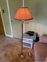Full view of the metal floor lamp showing the tall slim pole, round base and beige lampshade.