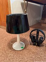Photo showing table lamp with black shade and white base, and Avantree headphones on stand on carpeted floor
