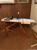 Full view of the ironing board with two irons on top, showing the padded cover and wooden legs.