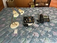 Overview of all three items on bed: vintage floral double lamp, black message device, and black landline phone