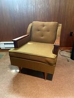 Front view of brown upholstered arm chair with wooden armrests and tapered legs.