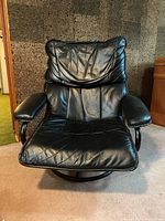 Front and angled side view of black upholstered lounge chair showing padded seat, back, and armrests with visible stitching and swivel base.