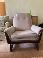 Front view of mid-century modern armchair with button-tufted back and wooden frame.