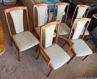 Six teak dining chairs in two rows, five armless and one with arms, light beige upholstery