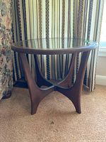 Side view of the round wood frame end table with sculptural legs and clear removable glass top.