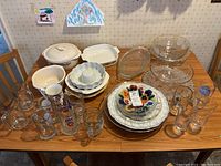 Full lot image showing various bowls, plates, mugs, steins, and bakeware arranged on a wooden table.