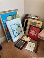 Group of various framed prints and a mirror leaning against the wall, showing different sizes and frame styles.