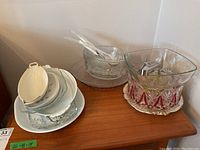 Initial image showing clear glass bowls, platters, white ceramic trays, and a few white serving utensils arranged together on a wooden surface.