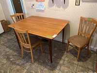 Overall view of the wooden MDF kitchen table with three wooden chairs placed around it on tiled flooring.