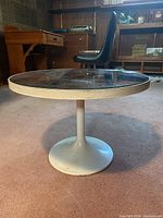 Side view of round end table showing white metal pedestal base and tabletop edge with some wear.