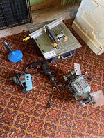 Overview photo of the tile cutter, drills, and bench grinder on a patterned carpeted floor.