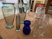 Overview of eight vases, varying shapes and colors including green, blue, and clear glass.