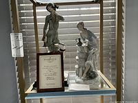 Two porcelain figurines side by side with framed certificate between them; certificate reads “Florence” model by Giuseppi Armani