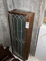 Stack of 6 vintage glass windows with wood frames leaning against a wall, showing tops and sides of frames.
