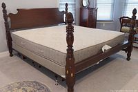 Side view of antique wooden bed frame showing carved rope-style posts, box spring with handles, mattress, and hardwood headboard.