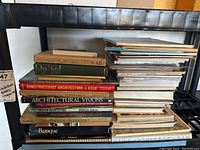 Photo showing a black shelving unit with a large stack of architectural books including Retrospect A45, The Country House, Constructivist Architecture in USSR, Architectural Visions, Post Modern Architecture, Southern Interiors, Baroque, and others.