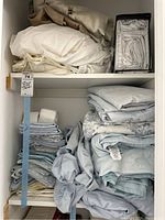 Shelves with folded king size bed sheets, pillowcases, and pillow protectors in white, beige, and blue tones.