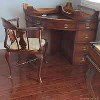 Wide view showing wooden corner desk with leather top and wooden corner armchair with upholstered seat, placed on a wood floor.