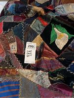 Close-up photo of patchwork sections featuring multiple fabric types and embroidery including a white flower applique on black fabric.