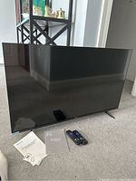 Photo showing a 38 inch Hisense Roku TV with two Roku remotes and manuals placed on carpet.