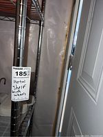 Close-up photo of metal wire frame with MaxSold label showing lot number 185 and description metal shelf with wheels.