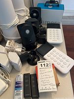 Multiple SimpleSafe black security cameras with mounts, white SimpleSafe keypad devices, motion sensor box and remote controls visible