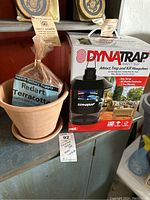 Photo showing Dynatrap insect trap box alongside Redart terracotta planter pot and matching saucer on a metal shelf.