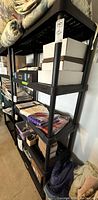 Black plastic utility shelf with various stored items such as boxes and textiles on shelves.