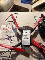 Falcon X25 drone top view showing red and black arms, propeller guards, and remote control on white table with manual.