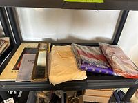 Shelf showing folded silk sarees, white fabric, historical books and documents, with a long mirror on the side.