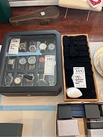 Full view of the black leather watch display case with 12 watches inside and wooden tray with watch band holders next to it, along with small jewelry boxes below.
